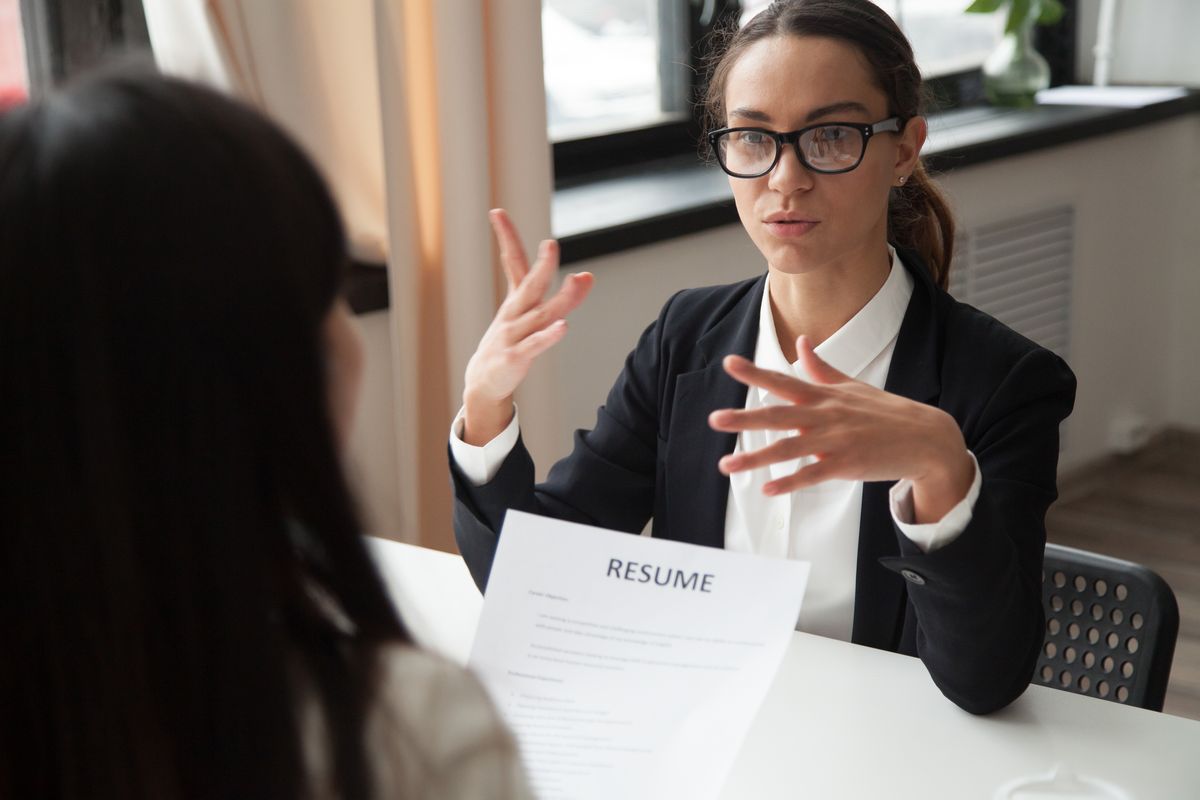 An interviewer explaining a point across the table while the candidate holds her résumé
